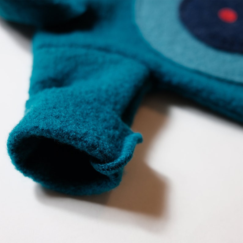 May include: A close-up of a teal blue fleece fabric with a rolled-up cuff. The fabric has a soft, fuzzy texture.