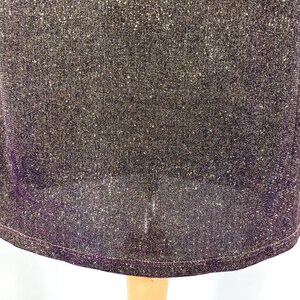May include: Close-up of a dark purple dress with a shimmering, textured fabric. The dress has a rounded hemline and a subtle sheen, suggesting a formal or evening wear garment. The fabric appears to be a knit or woven material.