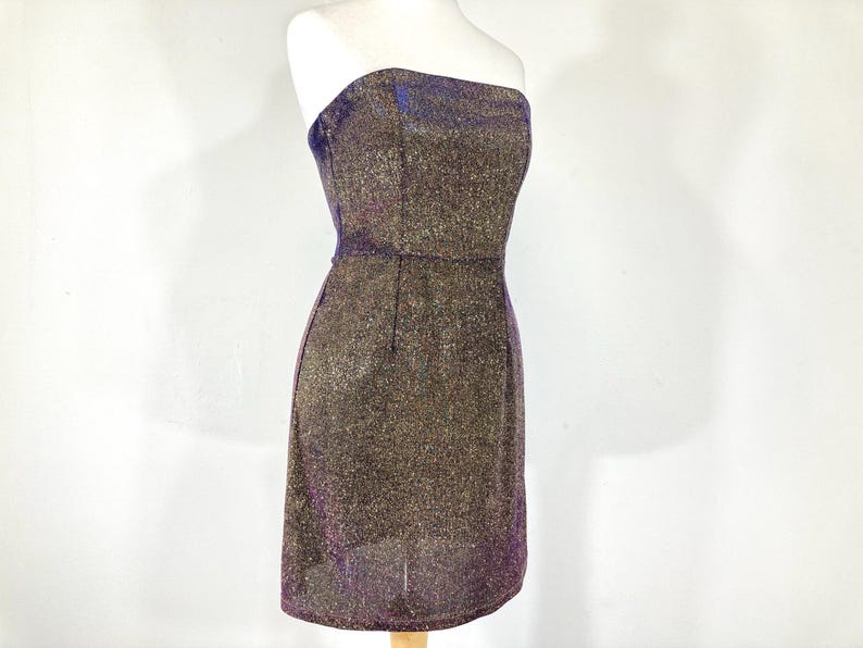 May include: A strapless, knee-length dress with a shimmering, textured fabric. The dress features a dark brown base with gold and purple metallic threads, creating a sparkling effect. The dress is displayed on a mannequin.