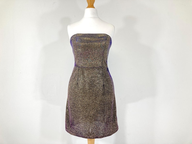May include: A strapless, knee-length dress with a shimmering gold and purple fabric. The dress is displayed on a mannequin against a white background. The dress has a fitted bodice and a slightly flared skirt, suitable for a party or special occasion.
