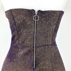 May include: A strapless, shimmering dress with a metallic finish. The dress features a full-length silver zipper down the front with a circular pull. The fabric has a speckled, glittery appearance.