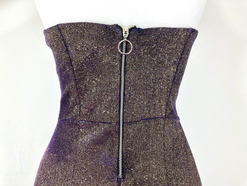 May include: A strapless, shimmering dress with a metallic finish. The dress features a full-length silver zipper down the front with a circular pull. The fabric has a speckled, glittery appearance.