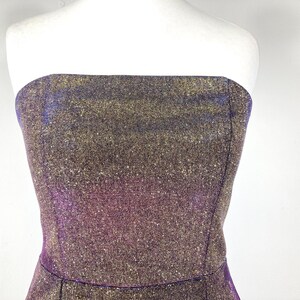 May include: A strapless dress with a shimmering, textured fabric. The dress features a blend of gold, purple, and blue hues, creating a sparkling effect. The bodice is fitted, and the dress appears to be a formal or party wear item.