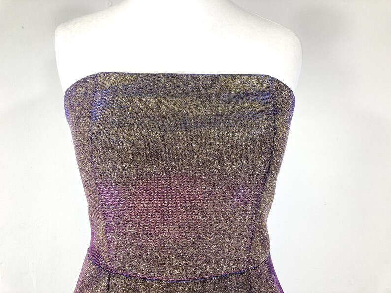 May include: A strapless dress with a shimmering, textured fabric. The dress features a blend of gold, purple, and blue hues, creating a sparkling effect. The bodice is fitted, and the dress appears to be a formal or party wear item.