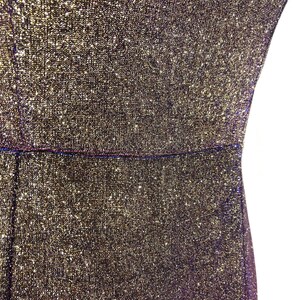 May include: Close-up of a shimmering, textured fabric in gold and black. The material appears to be a dress or garment, with a visible seam at the waist. The fabric has a sparkly, glittery appearance.