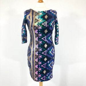 May include: A sequinned dress with a geometric pattern in black, gold, purple, and teal. The dress has long sleeves and a scoop neckline. The dress is displayed on a mannequin.