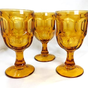 May include: Three amber-colored stemmed glasses with a textured, geometric design. The glasses have a rounded bowl shape and a sturdy base. The stem and base are the same color as the bowl. The glasses are arranged in a group, showcasing their design.