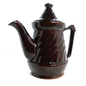 May include: A dark brown glazed ceramic teapot featuring a glossy finish, a distinct twisted or swirl pattern on the main body, a matching lid with a pointed finial, a curved spout, and an angular handle, set against a plain white background.