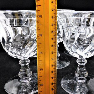 May include: Four clear glass stemmed wine glasses with a swirl pattern. The glasses are approximately 6 inches tall and are measured against a ruler.