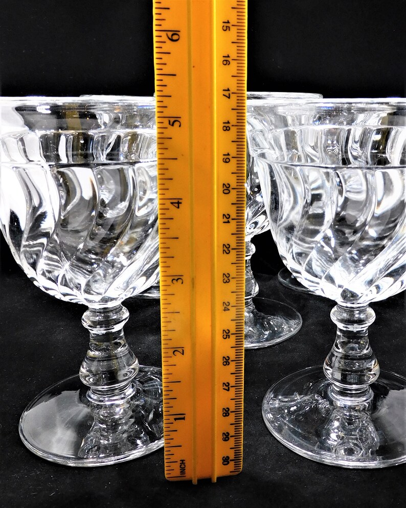 May include: Four clear glass stemmed wine glasses with a swirl pattern. The glasses are approximately 6 inches tall and are measured against a ruler.