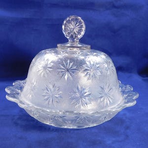 May include: A clear glass butter dish with a domed lid and a starburst pattern. The lid has a knob in the center.