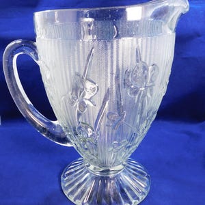 May include: Clear glass pitcher with a handle and a spout. The pitcher features a floral design and vertical textured stripes. The pitcher sits on a round, ribbed base. A classic piece for serving beverages.