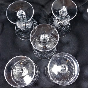 May include: Set of five clear glass stemmed drinking glasses with a swirl pattern. The glasses are empty and have a round base.