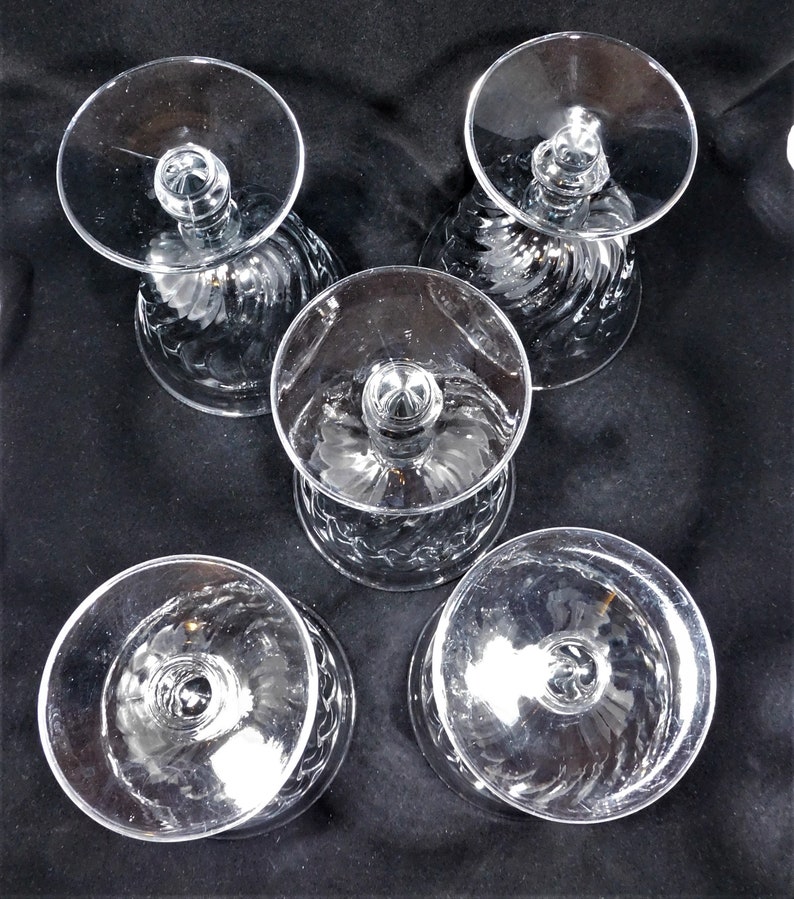 May include: Set of five clear glass stemmed drinking glasses with a swirl pattern. The glasses are empty and have a round base.