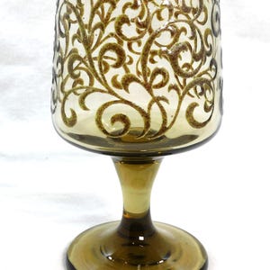 May include: A brown glass goblet with a gold swirl design. The goblet has a wide bowl and a tall stem.