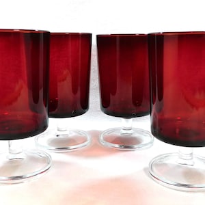 May include: Set of four red glass goblets with clear glass stems and bases. The goblets are all the same size and shape.