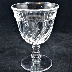 May include: A clear glass goblet with a swirling, textured design. The goblet has a wide bowl and a tall, slender stem.