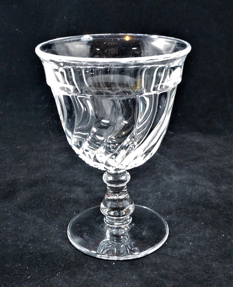 May include: A clear glass goblet with a swirling, textured design. The goblet has a wide bowl and a tall, slender stem.