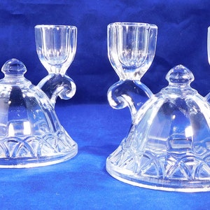 May include: Two clear glass candle holders with a decorative, ornate design. Each holder has three candle cups, with two on the sides and one in the center.