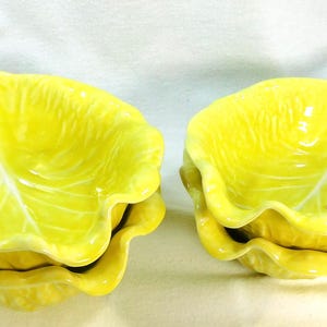 May include: Two ceramic leaf-shaped bowls in a bright yellow color. The bowls have a textured surface with a wavy edge, and are stacked on top of each other. The bowls are designed to resemble lettuce leaves.