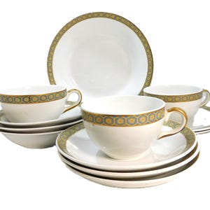 May include: A white porcelain tea set with gold trim and a geometric pattern in blue and yellow. The set includes teacups, saucers, and a serving bowl. The teacups have gold handles. The set is arranged on a white background.