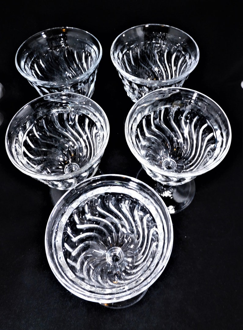 May include: Set of six clear glass dessert bowls with a swirl pattern. The bowls are empty and have a stemmed base.
