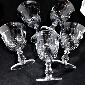 May include: Five clear glass wine glasses with a swirl design. The glasses are arranged in a cluster, with the stems pointing upwards.