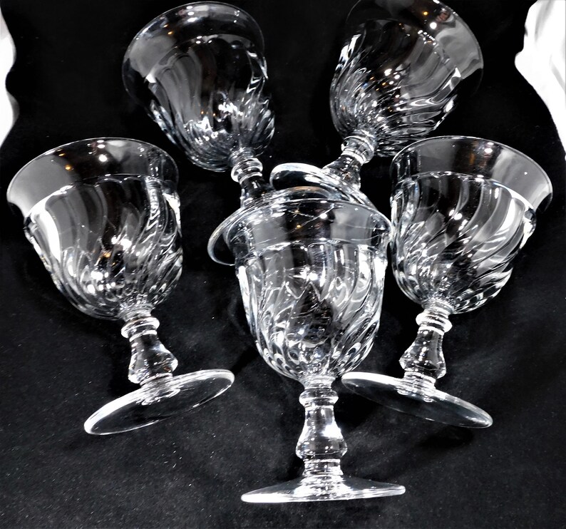 May include: Five clear glass wine glasses with a swirl design. The glasses are arranged in a cluster, with the stems pointing upwards.