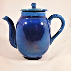 May include: A blue ceramic teapot with a lid. The teapot has a rounded body and a spout on the side. The handle is on the opposite side of the spout.