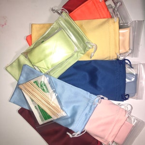 Op de afbeelding: Assortiment van kleurrijke microvezel brillenreinigingsdoekjes in verschillende kleuren, waaronder rood, oranje, geel, groen, blauw, roze en bruin. De doekjes zijn verpakt in doorzichtige plastic zakjes met een trekkoord.