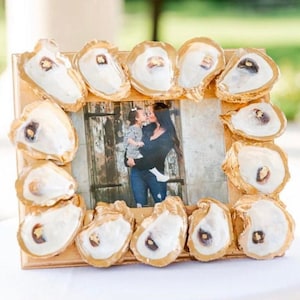 May include: A gold picture frame decorated with oyster shells, featuring a photo of a mother and daughter.
