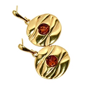 May include: A pair of gold-tone earrings with amber coloured stones set in the centre of each round disc. The discs have a textured, wavy design.
