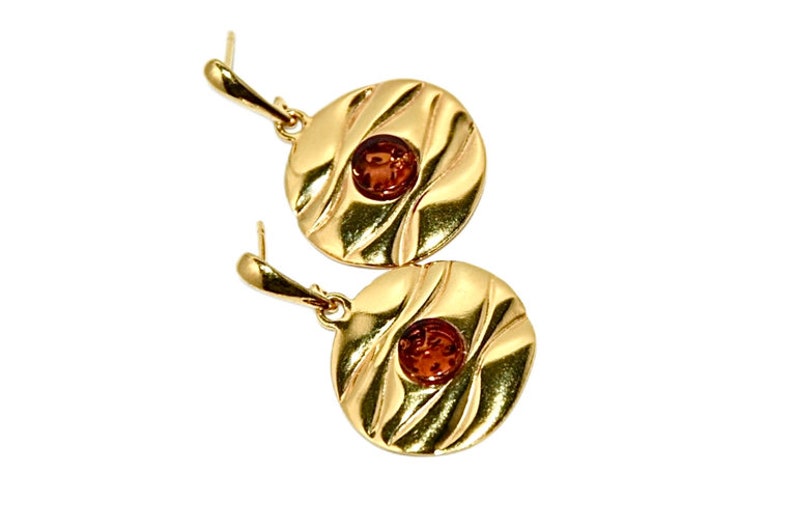 May include: A pair of gold-tone earrings with amber coloured stones set in the centre of each round disc. The discs have a textured, wavy design.