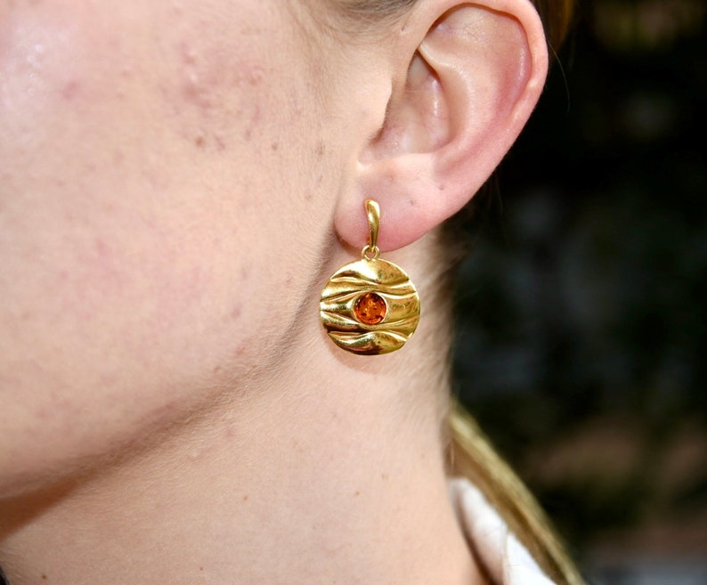 May include: Gold earrings with a round, textured design and a small amber stone in the centre.
