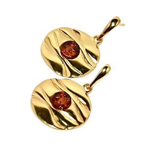 May include: A pair of gold earrings with a round, textured design and a small amber stone in the centre of each earring.