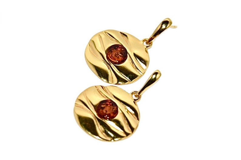 May include: A pair of gold earrings with a round, textured design and a small amber stone in the centre of each earring.