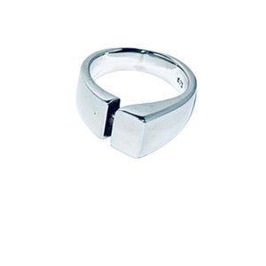 May include: A silver ring with a unique design. The ring features a split band with a rectangular accent on the front. The ring is made of a shiny, polished metal.