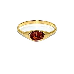 May include: A gold ring with a red gemstone set in a bezel setting.