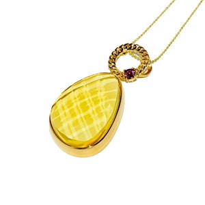 Puede incluir: Un collar de oro con un colgante amarillo en forma de lágrima y un pequeño acento de piedra preciosa rosa. El colgante tiene un diseño delicado y estampado.