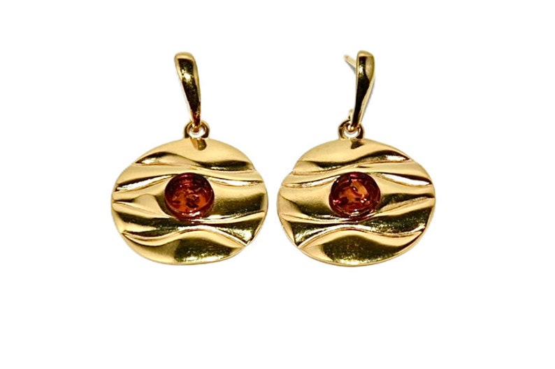 May include: A pair of gold earrings with a round, textured design. Each earring features a small, round amber stone in the centre.