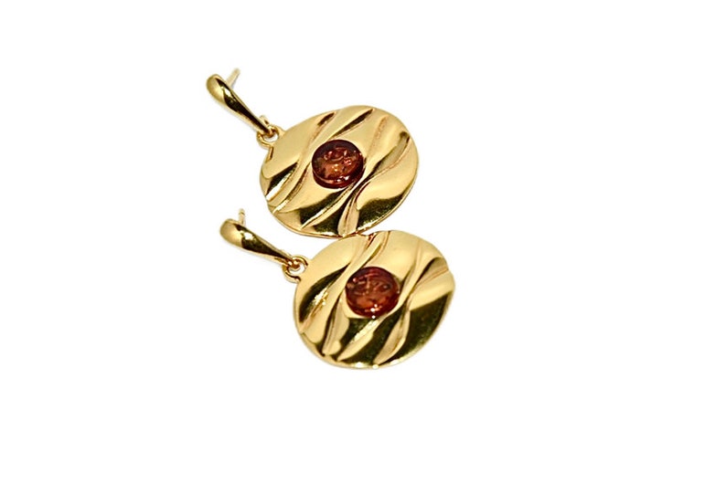 May include: A pair of gold earrings with a round, textured design and a small, round, amber-coloured stone in the centre of each earring.