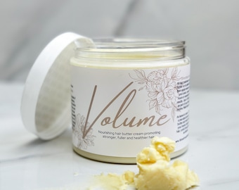 May include: A white jar with a white lid containing a yellow hair butter cream. The jar has a label that says "Volume Nourishing hair butter cream promoting stronger, fuller and healthier hair". There is a dollop of the cream on a white surface.