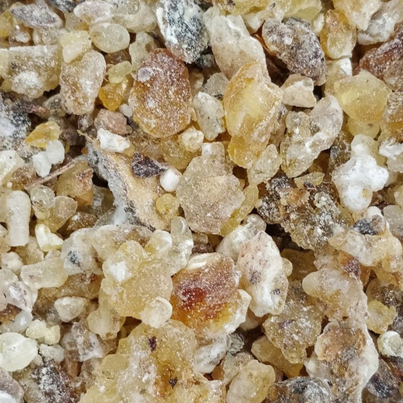 May include: Close-up of a pile of small, translucent, amber-colored resin pieces. The resin is irregularly shaped and has a slightly rough texture.