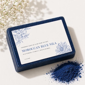 May include: A dark blue soap bar with a white label featuring floral illustrations and the text "MOROCCAN BLUE NILA". The bar is 3.5 oz. A pile of blue powder is next to the soap. The soap is handmade.