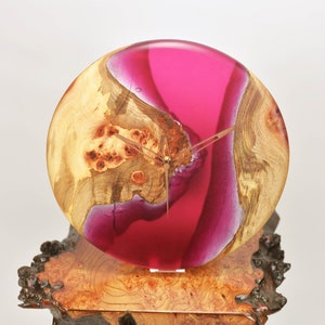May include: A pink and wood resin clock with gold hands. The clock is mounted on a wooden base.
