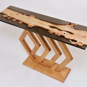 Può includere: Un tavolo rettangolare lungo con un piano in resina epossidica nera e una base in legno naturale. Il piano del tavolo presenta un'unica venatura del legno. La base è composta da quattro pezzi di legno a forma di diamante.