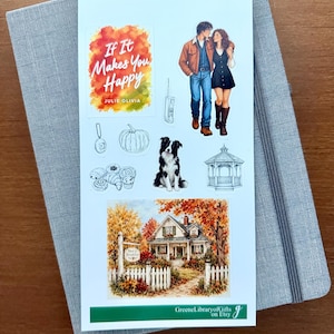 May include: A sticker sheet featuring a watercolor-style illustration of a house, a couple walking, a border collie, a pumpkin, pastries, a gazebo, and a text graphic that reads If It Makes You Happy by Julie Olivia, placed on a gray notebook.