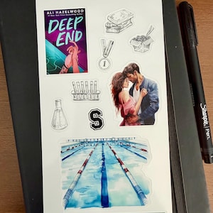 May include: A collection of stickers featuring book covers, illustrations, and text. The stickers include a book cover with the title "Deep End", a swimming pool, a medal, and a couple embracing. A black pen rests on a black notebook.