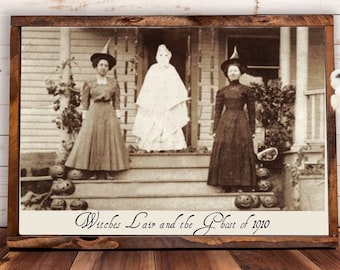 May include: A framed black and white photograph of two women dressed in costumes for Halloween. The women are standing on a porch with a ghost figure in the middle. The text below the image reads "Witches Lair and the Ghost of 1910".