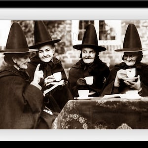 May include: Four women wearing black pointed hats and cloaks are sitting at a table drinking tea. They are all smiling and appear to be enjoying themselves.